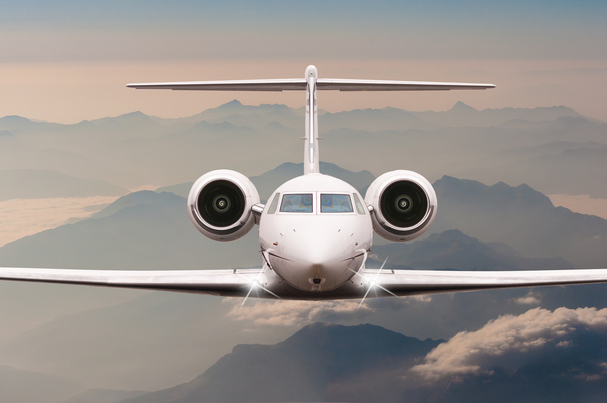 Airplane fly over clouds and Alps mountain on sunset. Front view of a big passenger or cargo aircraft, business jet, airline. Transportation, travel concept